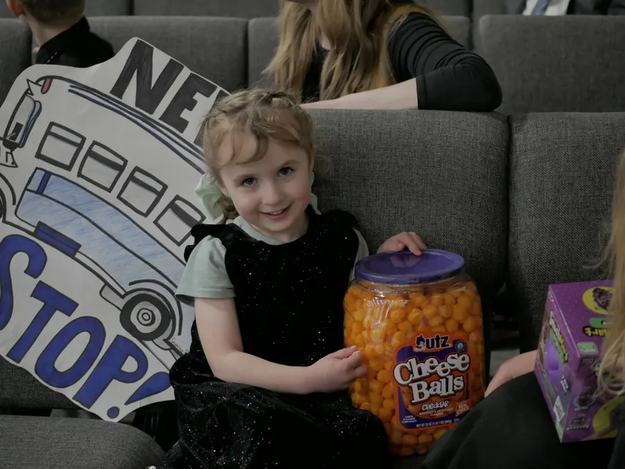 A little girl smiling beside her prize and a bus-shaped sign