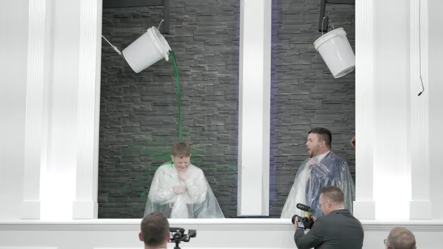 Two people in rain ponchos as a bucket of green slime tips over them